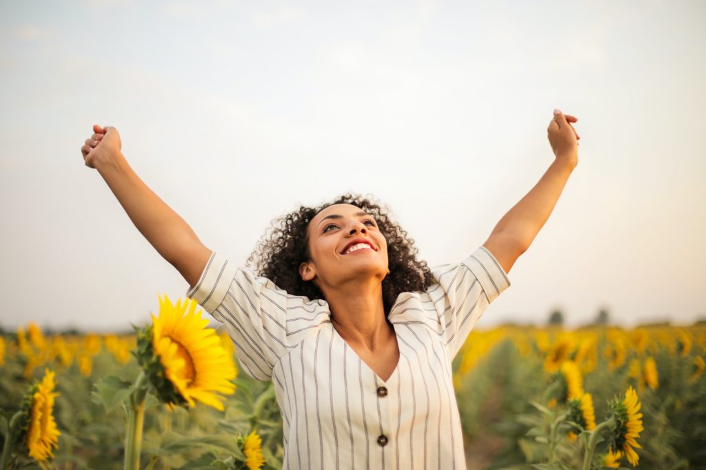 woman standing in front of sunflowers with arms raised