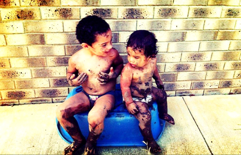 Two muddy boys sitting on an upturned bath tub
