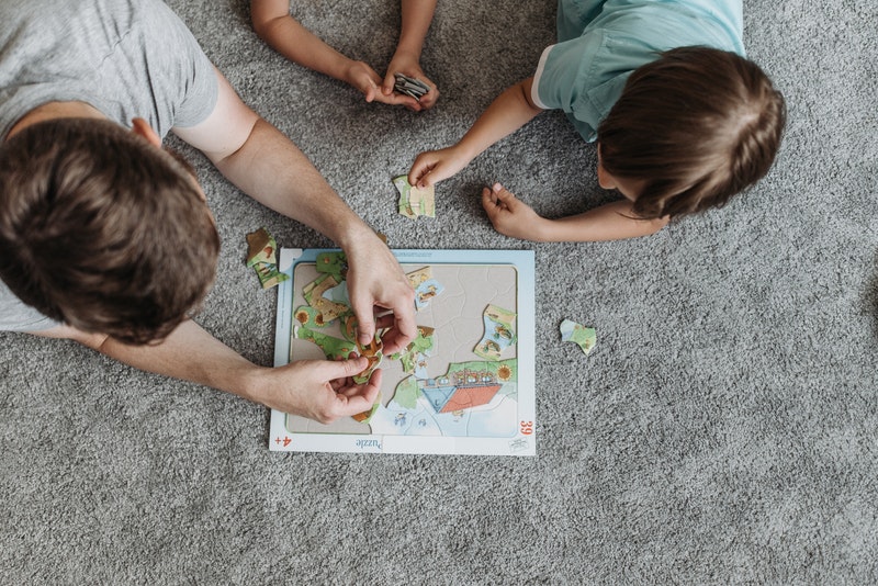 three children solving a jigsaw puzzle on a carpeted floor. things to do with kids - puzzles