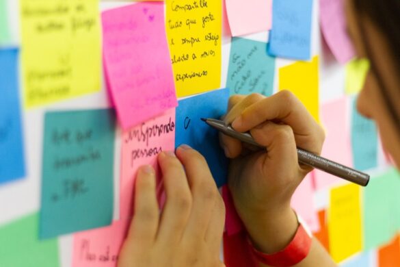 Wall of colourful post-it notes. A young person is writing on one.