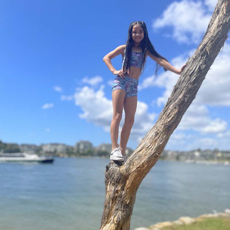 Young girl in activewear standing on tree with water in the background