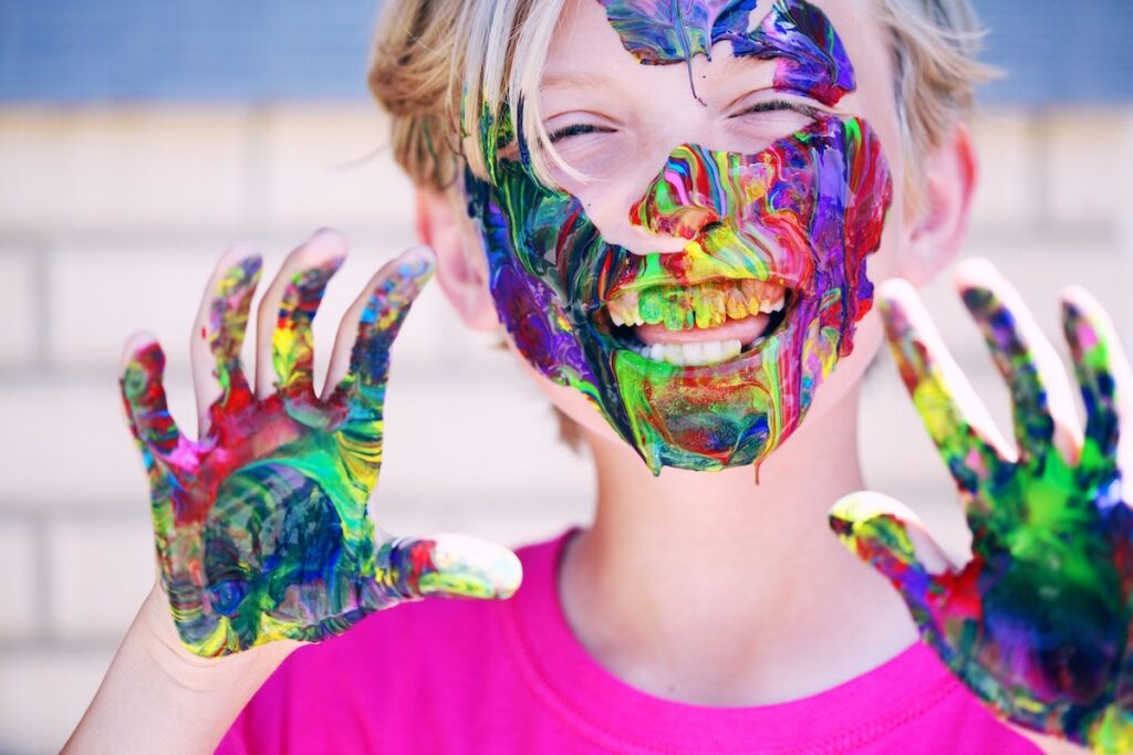 Smiling child with paint smeared on face and all over hands