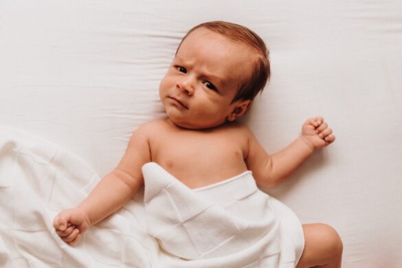 Baby lying on bed with sheet cover body and a puzzled expression on their face