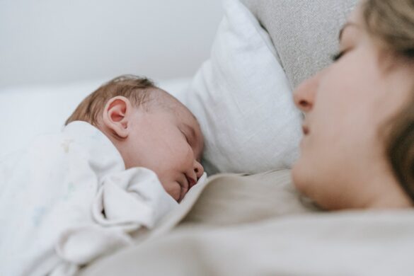 woman lying in bed looking at sleeping newborn