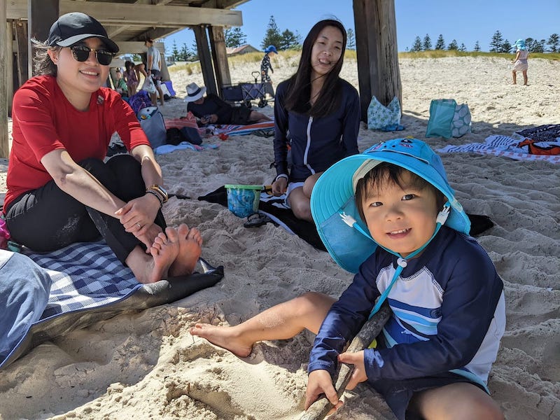 Two women and one boy sitting in the shade at the beach, smiling.