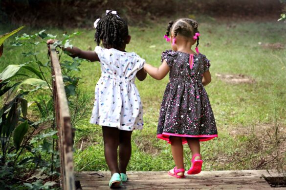 The backs of two Black young girls walking hand in hand up some stairs.