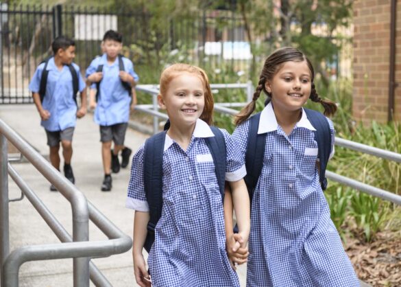Female primary school students wearing blue gingham dresses with boys in background