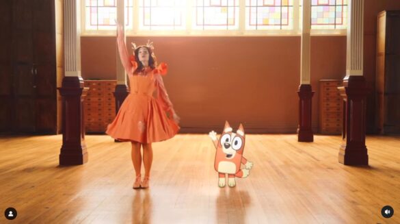 Emma Memma and Bingo Heeler standing side by side with arms raised in a wave. They are in a dance studio with sunlight streaming onto the wooden floors.