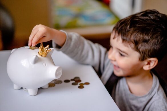 Young boy smiling and putting coins into a white piggy bank