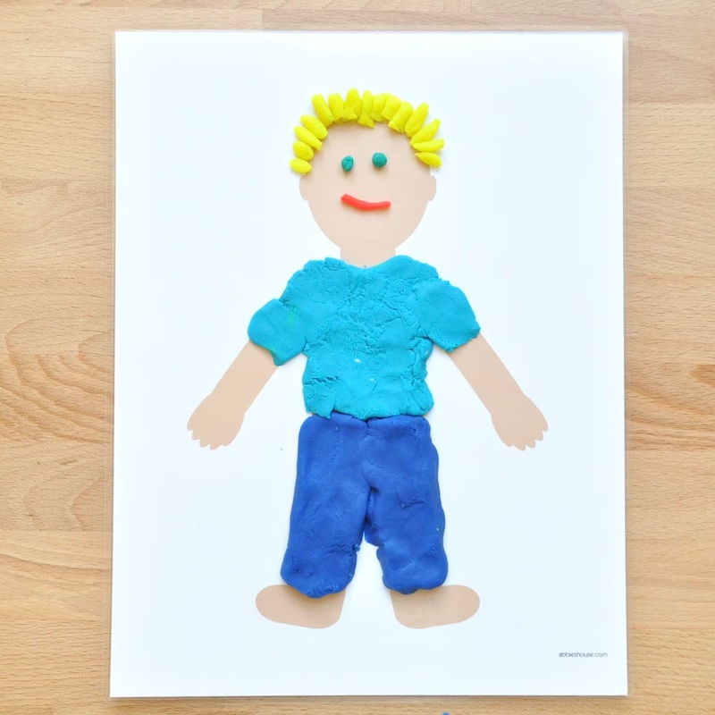 White piece of paper with a blank beige-coloured outline of a body. Play dough has been used to create clothes, hair and facial features