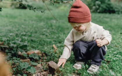 Young child squatting on a grass lawn touching a piece of rock.