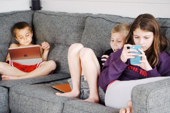 Three primary-aged children sitting on the couch, each engrossedly looking at their device.