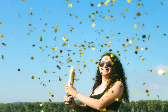 Smiling young woman standing in a field after releasing a confetti cannon.