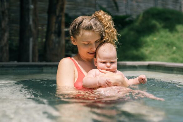 Woman in a shallow pool carrying a baby.